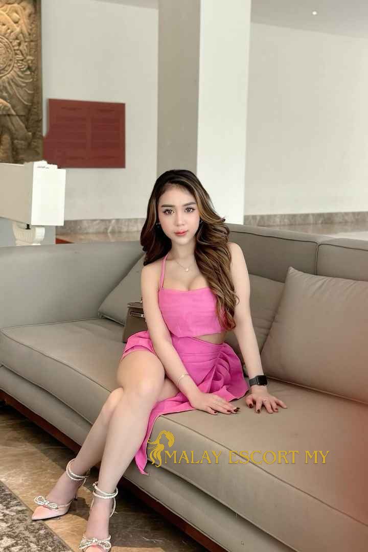 Attractive Malay woman in pink dress sitting on a couch. Malay Escort My